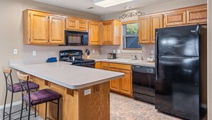 A kitchen with wooden cabinets, a black refrigerator, a stove, and a sink.