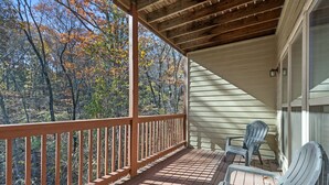 A covered porch with a wooden railing, two Adirondack chairs, and a view of autumn foliage.