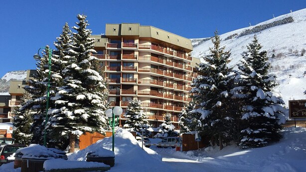 Ein mehrstöckiges Hotel mit Balkonen, umgeben von schneebedeckten Bäumen und einem Berg im Hintergrund.