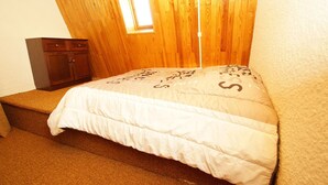 Ein Schlafzimmer mit Holzbalkendecke, einem kleinen Fenster, einem Bett mit weißer Daunendecke und einem hölzernen Kleiderschrank.