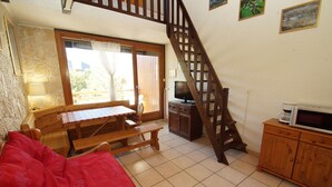 Ein gemütliches Wohnzimmer mit einer Holztreppe, einem Fernseher und einem Essbereich mit Tisch und Bänken.