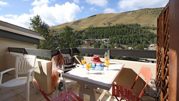 Un balcón con mesa lista para dos personas, dos sillas y vistas a un paisaje montañoso.