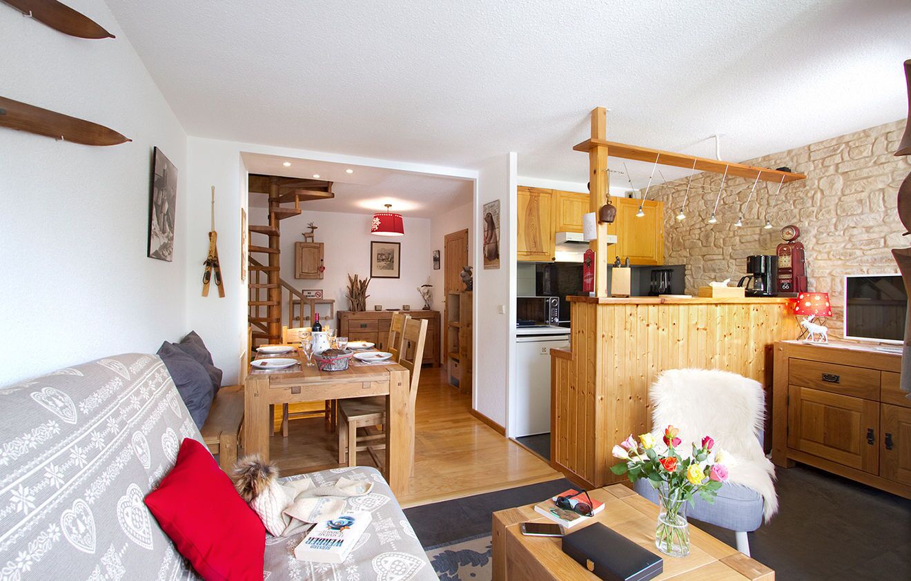 Un salon chaleureux avec un canapé, une table à manger et un coin cuisine doté de meubles en bois et d’un mur en pierre.