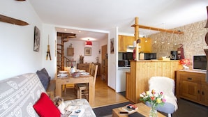 Una sala de estar acogedora con sofá, mesa de comedor y zona de cocina con armarios de madera y pared de piedra.
