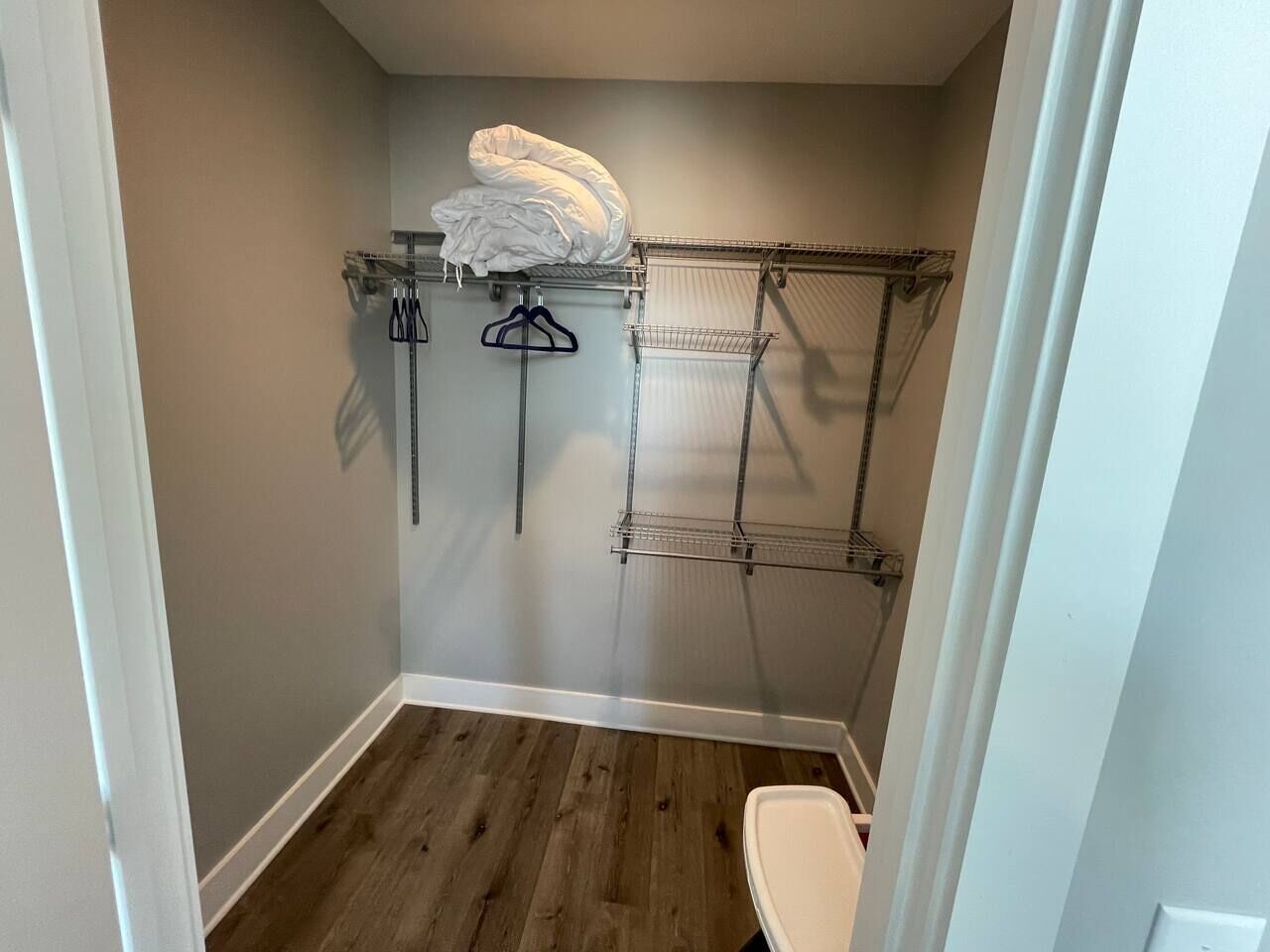 A small bathroom with a wooden floor, a white toilet, and a metal towel rack with a white towel.