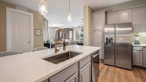 A modern kitchen with a marble countertop, stainless steel appliances, and pendant lighting.