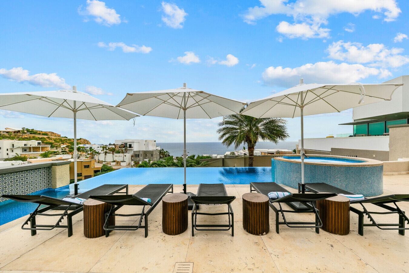 A rooftop infinity pool with lounge chairs and umbrellas, overlooking a coastal landscape.
