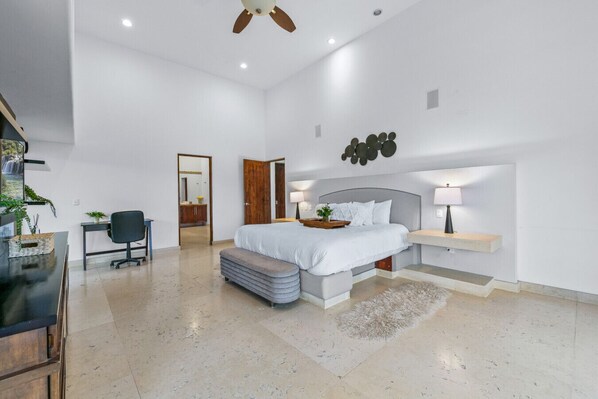 A modern bedroom with a bed, bedside table, lamp, and a desk with a chair.