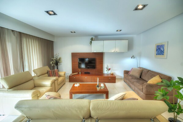 A modern living room with a beige sofa set, a wooden coffee table, a brown sofa, a flat-screen TV mounted on a wooden cabinet, and a potted plant. - Large & modern 3bedroom in prime location WPAC1-1 (St Julian's)