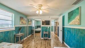 A bedroom with a ceiling fan, a bed, a dresser, a mirror, and a painting on the wall. - Peacock Paradise (Holmes Beach)