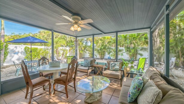 A covered patio with a ceiling fan, a round glass table, wooden chairs, a sofa, and a blue umbrella. - Peacock Paradise (Holmes Beach)