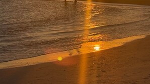 A beach scene with the sun setting over the ocean, people walking along the shore, and waves gently lapping at the sand. - Peacock Paradise (Holmes Beach)