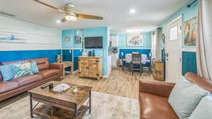 A living room with a brown leather sofa, a wooden coffee table, a ceiling fan, and a television. - Peacock Paradise (Holmes Beach)
