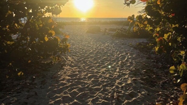 Un sentier menant à une plage, avec un coucher de soleil en arrière-plan.