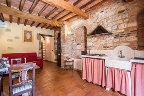 A rustic kitchen with stone walls, a red sofa, a wooden table with a vase, and a tiled floor. - Apartment 'Agriturismo Ischieto - La Cantina' with Shared Pool, Wi-Fi, and Air Conditioning (Rapolano Terme)