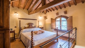 A bedroom with a wooden bed, a stone fireplace, and a window with a view. - Apartment 'Agriturismo Ischieto - La Torretta' with Shared Pool, Wi-Fi and Air Conditioning (Rapolano Terme)