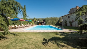 A swimming pool with lounge chairs and umbrellas, surrounded by greenery and a stone building. - Apartment 'Agriturismo Ischieto - La Torretta' with Shared Pool, Wi-Fi and Air Conditioning (Rapolano Terme)