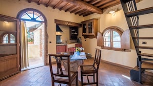 A rustic kitchen with wooden beams, a dining table with chairs, and a view through an open door. - Apartment 'Agriturismo Ischieto - La Torretta' with Shared Pool, Wi-Fi and Air Conditioning (Rapolano Terme)