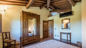 Ein Schlafzimmer mit einem großen Holzschrank, einem Bett mit floralem Überwurf, einem Holzstuhl und einem kleinen Tisch.