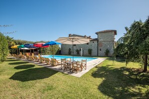 Un espace piscine avec des chaises longues et des parasols, un bâtiment en pierre et une pelouse bien entretenue.