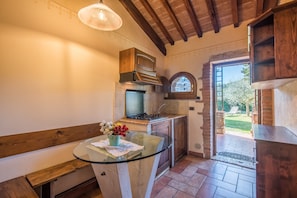 A kitchen with a glass table, wooden cabinets, a built-in oven, and a view to the outside. - Holiday Home "Agriturismo Ischieto - Il Pino" with Shared Pool and Wi-Fi (Rapolano Terme)