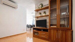 Een woonkamer met een televisie, een houten kast en een eethoek met stoelen.