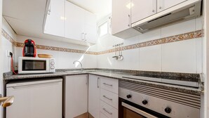 Een compacte keuken met witte kastjes, een magnetron, een kleine koelkast en een gasfornuis.