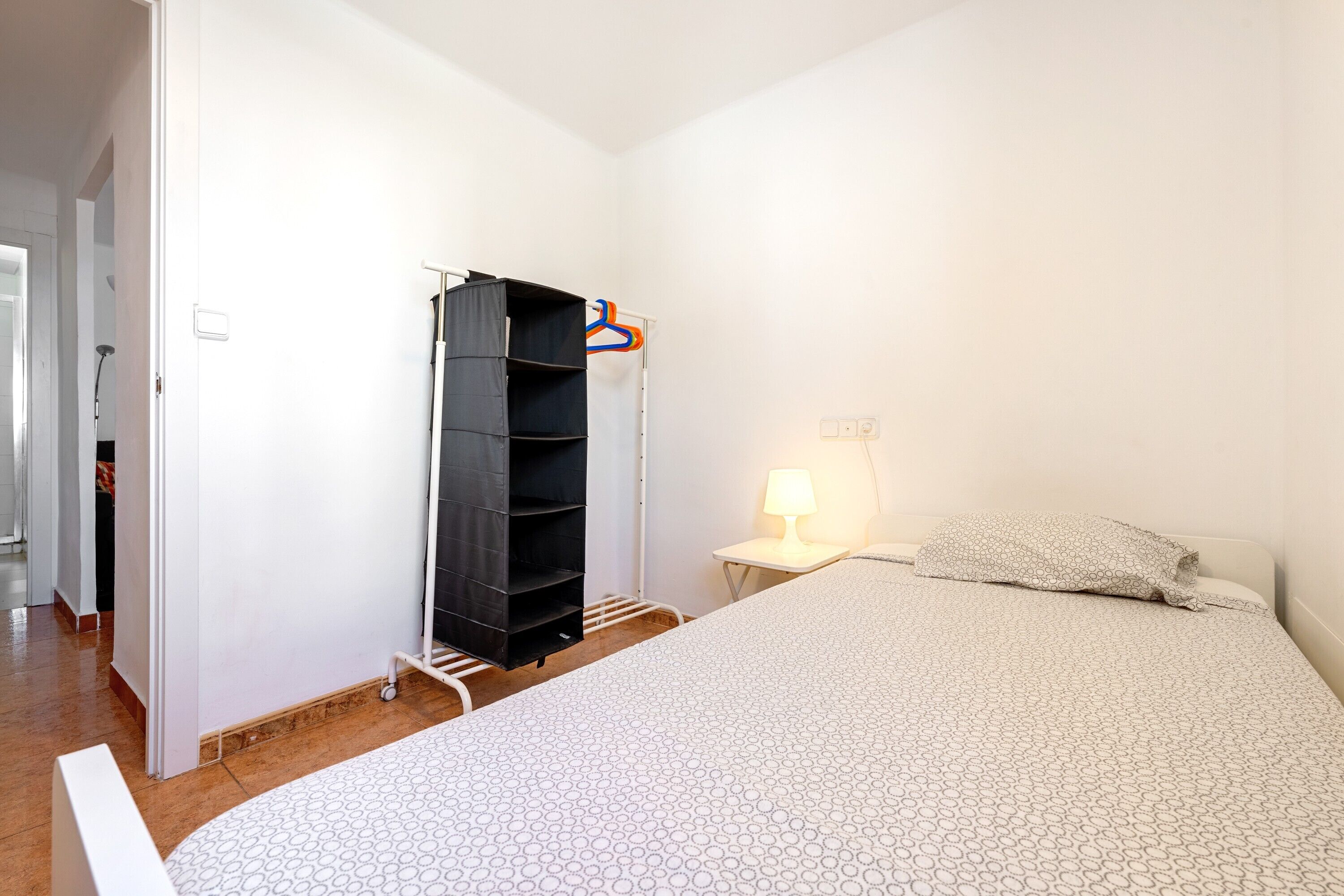 A bedroom with a bed, a wardrobe, a nightstand, and a lamp.