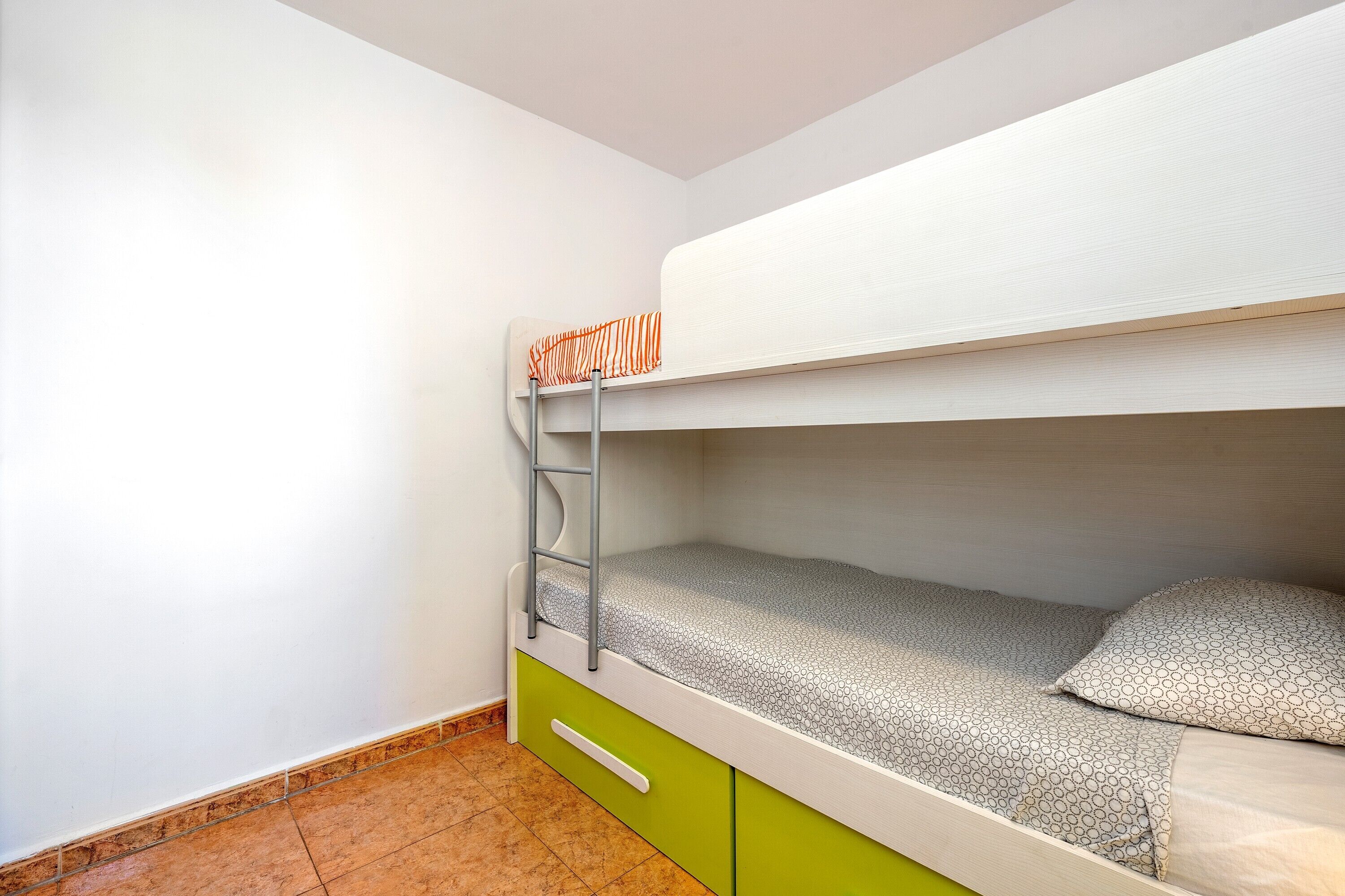 Una cama litera con una escalera, un cajón verde y una pared blanca.
