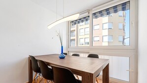 Een eetgedeelte met een houten tafel, zwarte stoelen, een blauwe vaas en uitzicht op een gebouw door een raam.