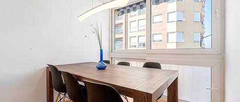A dining area with a wooden table, black chairs, a blue vase, and a view of a building through a window.