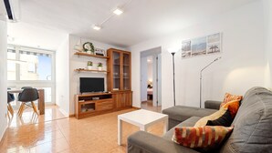 Een woonkamer met een bank, een televisie, een kast en een eethoek met stoelen.