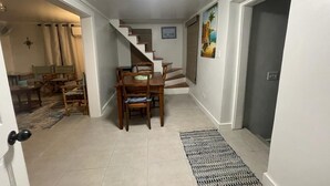 Un pasillo con una escalera que lleva a un comedor con mobiliario de madera y un cuadro en la pared.
