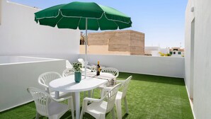 Une terrasse sur le toit, avec un parasol vert, des chaises blanches, une table et un pot de fleurs.