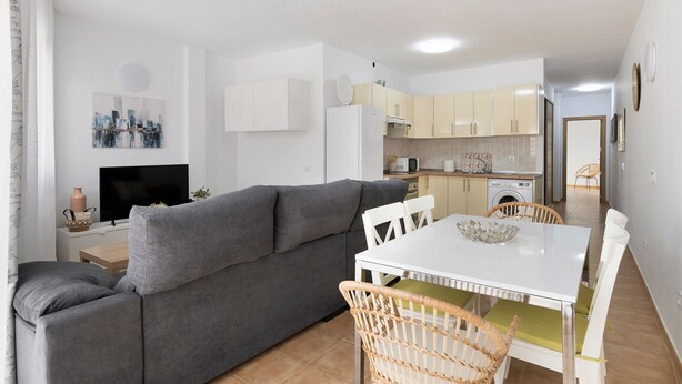 Un salon moderne avec un canapé gris, une table à manger blanche et des chaises en osier.