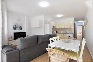 A modern living room with a grey sofa, white dining table, and wicker chairs.