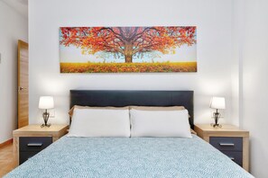 Un dormitorio con una cama grande, dos mesitas de noche con lámparas, un cabecero y un cuadro de un árbol colgado en la pared.