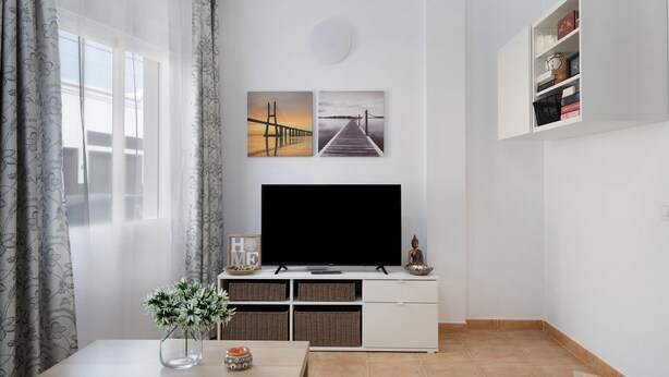 Un salon avec un téléviseur, un meuble blanc et des œuvres d’art accrochées au mur.