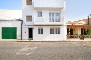 A two-story building with a white facade, a green door, and a balcony with a railing.