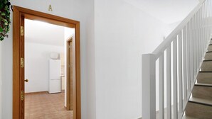 Un escalier avec des rampes blanches, une porte en bois dotée d’une poignée en laiton et un sol carrelé.
