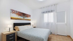 Une chambre à coucher avec un lit, une table de chevet avec une lampe, une fenêtre avec des rideaux et un tableau au mur.