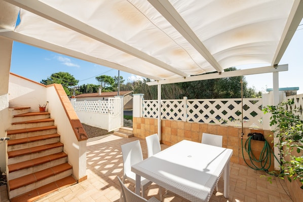 Un porche cubierto con una mesa y sillas blancas, una escalera y una manguera de jardín.