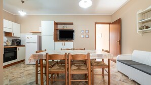 Una cocina compacta con una mesa de comedor, sillas, un refrigerador, una estufa y un televisor.