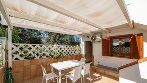 Un patio exterior con una mesa y sillas blancas, una cerca blanca y una ventana con contraventanas de madera.