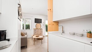 A modern kitchen with white cabinets, a wooden accent wall, a dining area with a round table, and a television mounted on the wall.