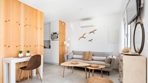 A modern living room with a white sofa, wooden dining table, and a small kitchen area.