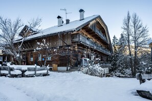 Un chalet en bois doté d’un balcon, entouré de paysages enneigés, et sous un ciel dégagé.