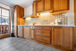 Une cuisine avec des meubles en bois, un pare-feu en carreaux et une fenêtre donnant sur des montagnes enneigées.