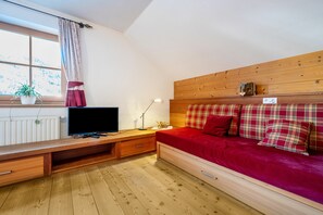 Una habitación con una cama de madera, televisor, escritorio y ventana con cortinas.