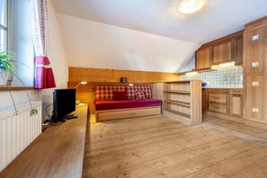 Une pièce de taille modeste avec un plancher en bois, un canapé recouvert d’une couverture à carreaux, un téléviseur et des meubles en bois.